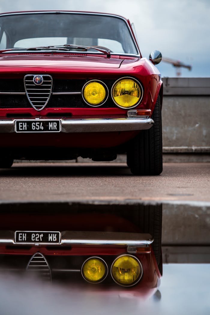 Front view of a classic red Alfa Romeo car with yellow headlights reflecting on a wet surface.