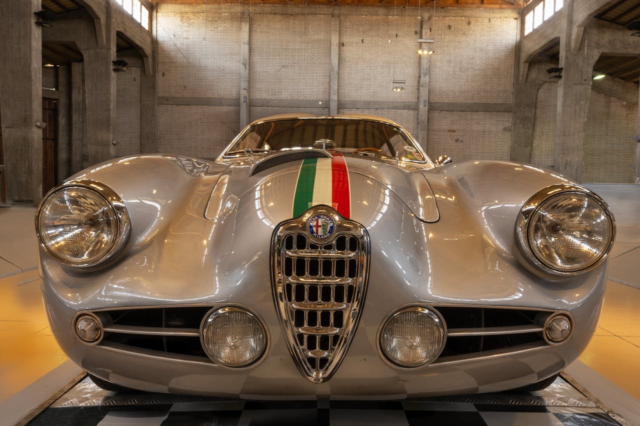 Front view of a vintage silver Alfa Romeo car inside an industrial garage setting.